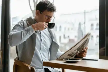 Smartphone mostrando feed de noticias junto a diarios impresos en un escritorio