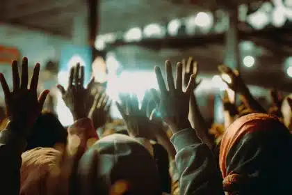 Multitud de asistentes a un festival musical al aire libre con las manos levantadas bajo luces de escenario