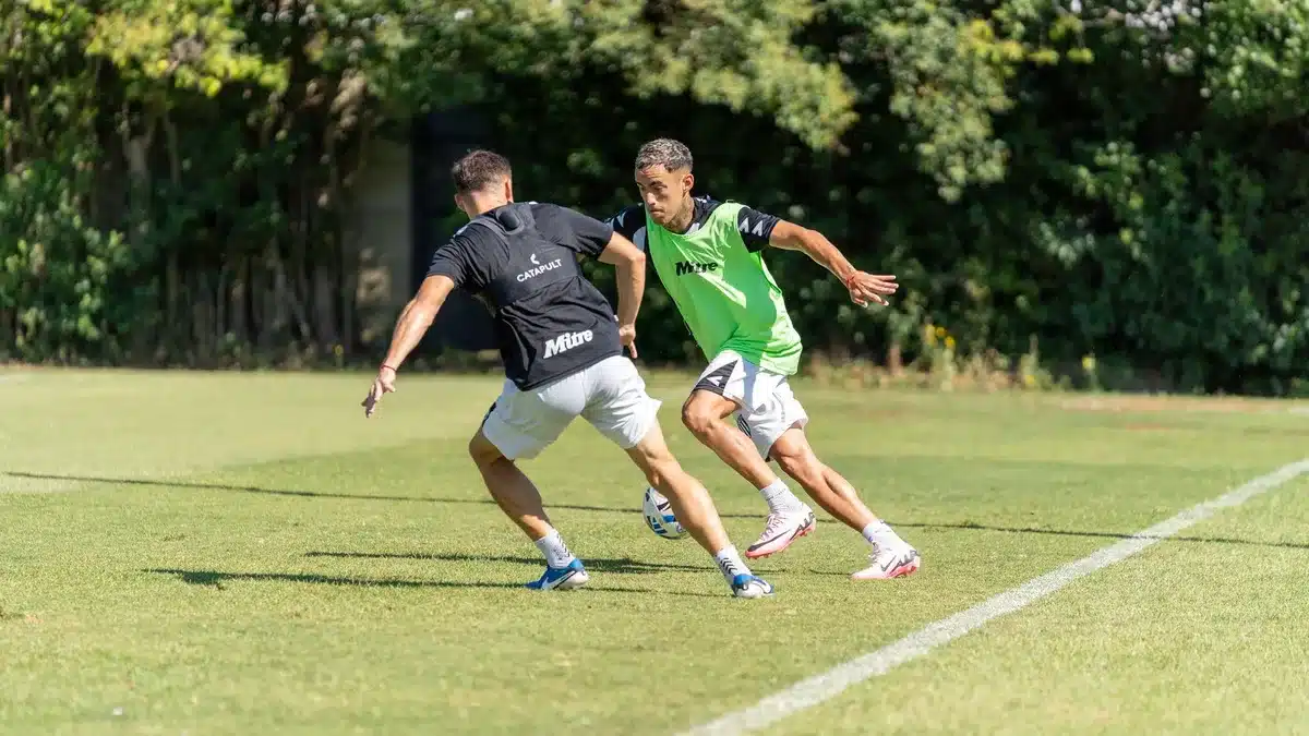 Equipo de fútbol en sesión de entrenamiento con jugadores realizando ejercicios tácticos.