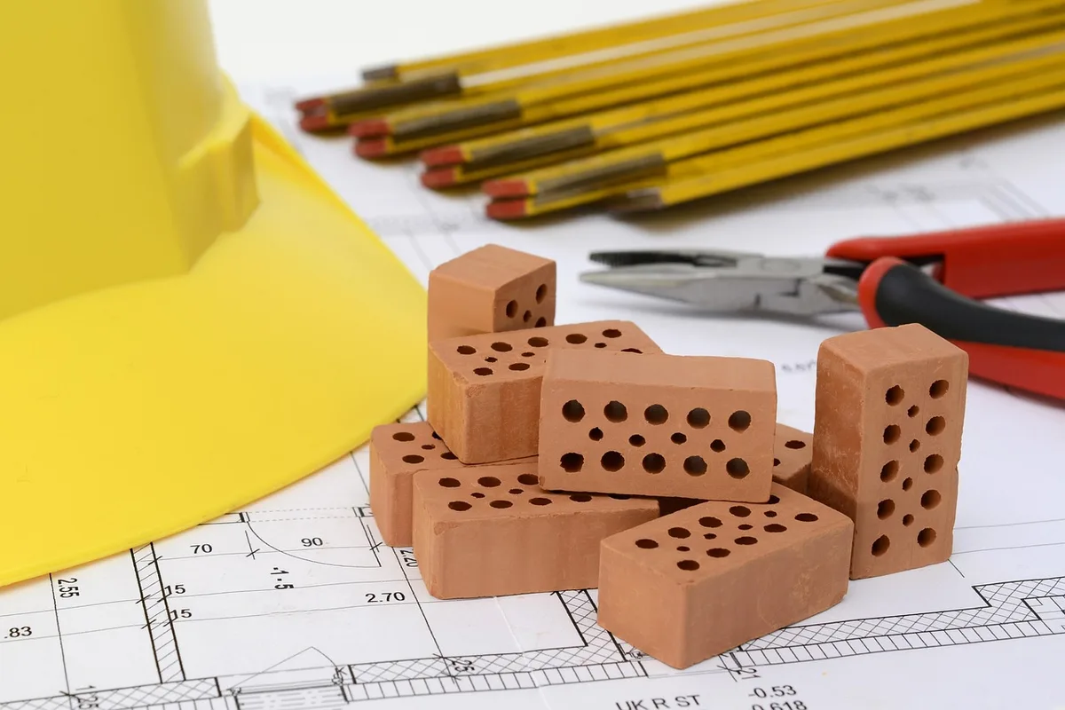 Manos sobre planos de renovación y calculadora que ilustran decisiones financieras