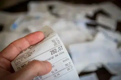 Manos anónimas sobre una mesa con billetes, calculadora y pantalla con gráficos cambiarios