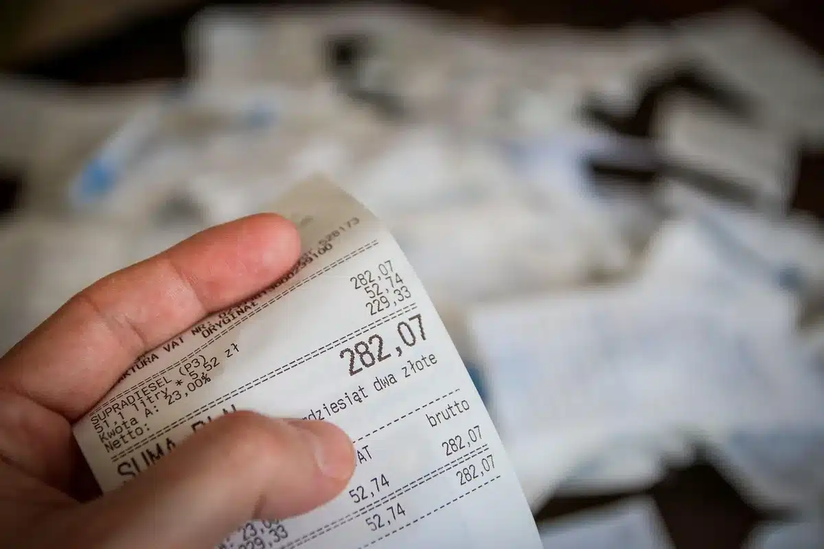 Manos anónimas sobre una mesa con billetes, calculadora y pantalla con gráficos cambiarios