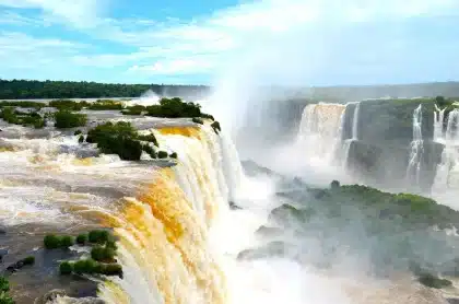 Pasarelas del parque con visitantes anónimos y caída de agua al fondo, vista amplia